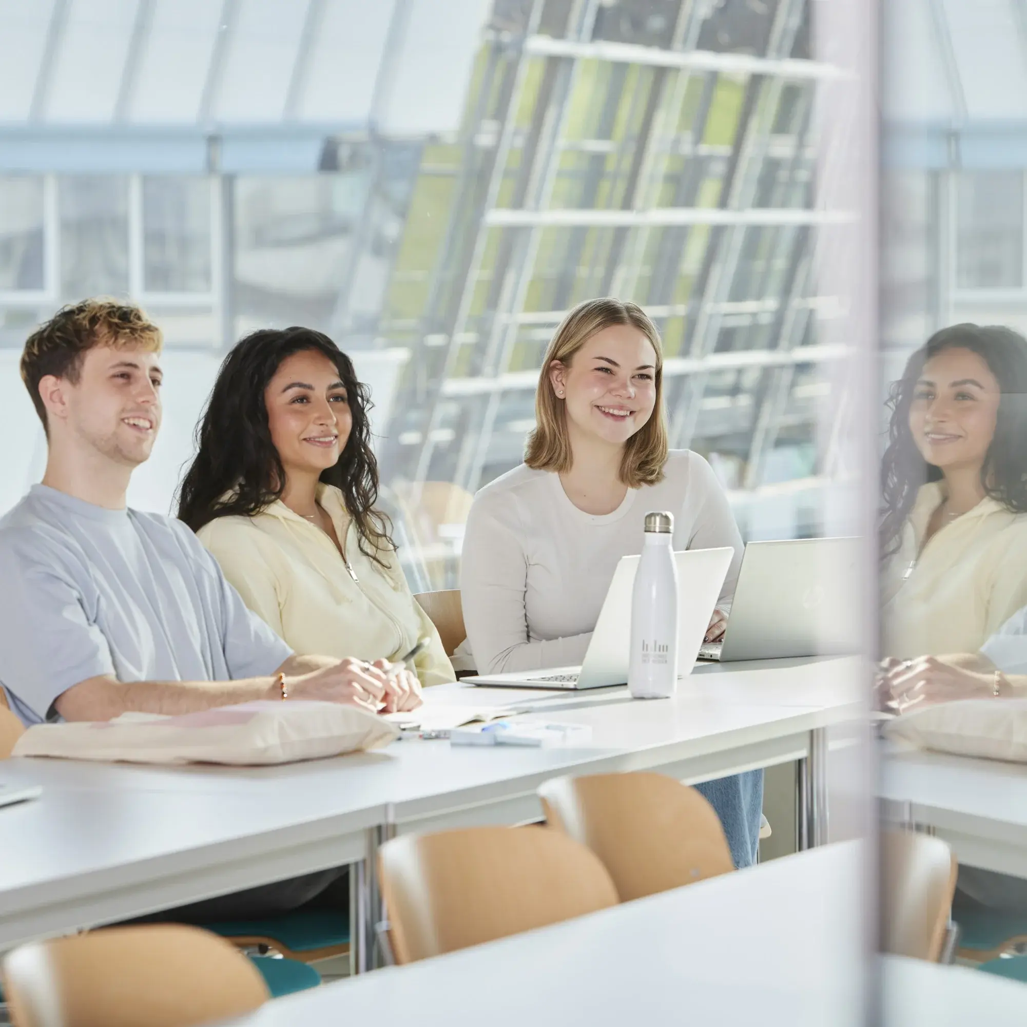 Drei Studierende sitzen in einem hellen Vorlesungsraum und arbeiten.